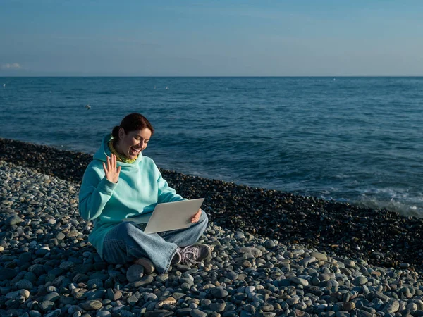 Femme caucasienne communiquant par appel vidéo sur ordinateur portable sur la plage de galets. — Photo