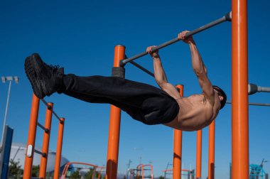 Açık havada üstsüz bir adam yatay barda beyaz giyiniyor.. 