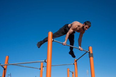 Çıplak gövdeli bir adam yatay çubukta denge sağlar.. 