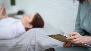 Bir kadın psikoterapist bir hastayla seans sırasında tablete not alır. Kafkasyalı kadın psikoloğun kanepesinde yatıyor.. 