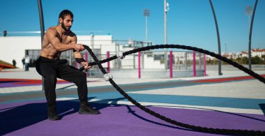 Gömleksiz adam dışarıda halatla egzersiz yapıyor.. 