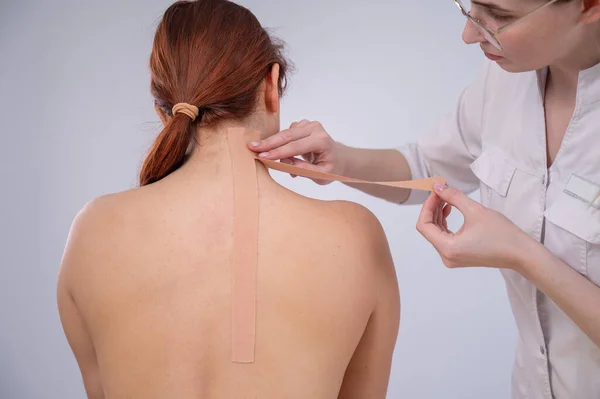 Female doctor glues kinesio tapes on the patients shoulder.