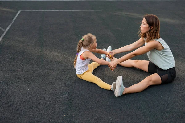 Mor og datter går ind til sport udendørs. Kaukasiske kvinde og lille pige er engageret i fitness på stadion. - Stock-foto