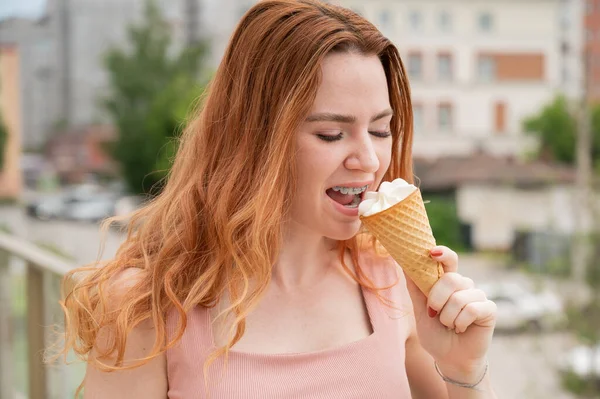 Retrato de jovem bela mulher ruiva sorrindo com aparelho e indo comer cone de sorvete ao ar livre no verão — Fotografia de Stock