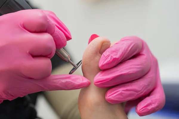 Bir pedikür uzmanı, güzellik salonunda aşındırıcı diski olan bir makine kullanan bir müşterinin ayak parmaklarını tedavi eder.. — Stok fotoğraf