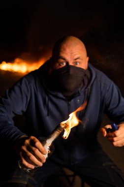 Maskeli bir adam yanan bir şişe tutuyor. Molotof kokteyli.