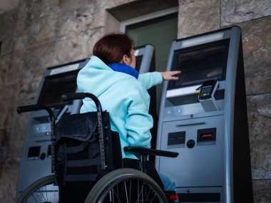 Tekerlekli sandalyedeki beyaz bir kadın tren istasyonundaki self servis kasasına ulaşamaz. Ulaşılması zor bir ortam.