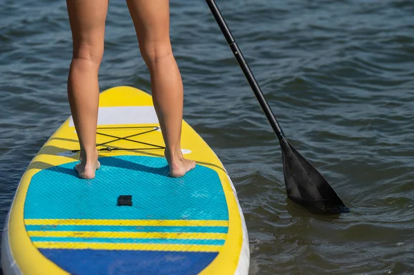 Fehér nő úszik egy SUP táblán. A női lábak közelsége a szörfözésen. — Stock Fotó