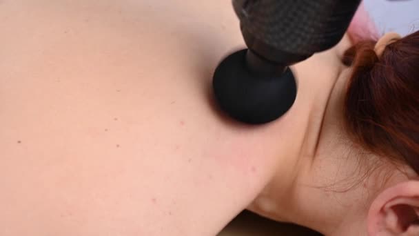 Doktorn masserar ryggen på en kvinnlig patient med en slagmassagepistol. — Stockvideo
