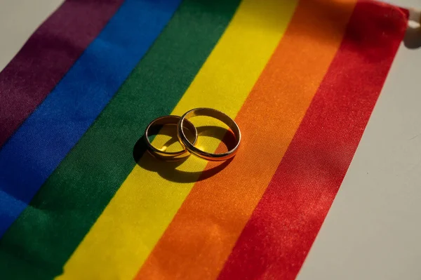 Legalización de matrimonios entre personas del mismo sexo. Bandera de arco iris y anillos de boda. —  Fotos de Stock