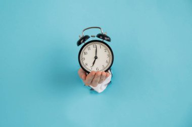 Bir kadın mavi kağıttan bir arka planda bir delikten dışarı çıkar ve çalar saati tutar. Boşluğu kopyala