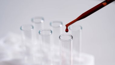 Laboratuvar asistanının beyaz arka plandaki bir test tüpüne kan damlatırken yakın plan fotoğrafı.