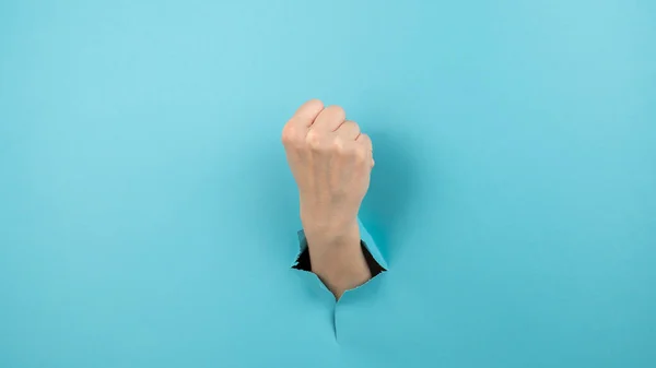 青い背景から穴から突き出た女性の手が拳を示す — ストック写真