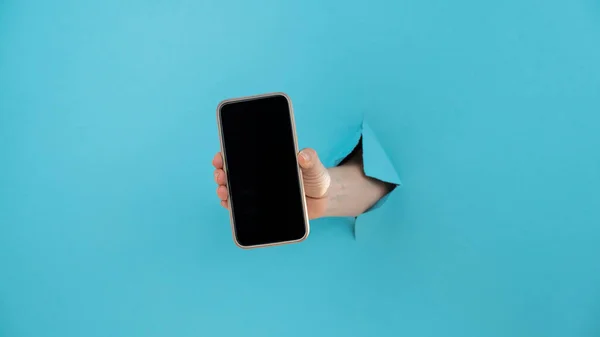 Una Mano Femenina Que Sobresale Agujero Fondo Azul Sostiene Teléfono — Foto de Stock