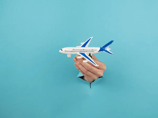 A female hand sticking out of a hole from a blue background holds a model of an airplane