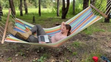 Ormandaki bir hamakta otururken dizüstü bilgisayarda çalışan beyaz bir kadın. Yürüyüşte kablosuz bilgisayar kullanan bir kız.