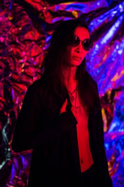 Stüdyoda neon ışıklı güneş gözlüklü bir transseksüel modelin portresi.