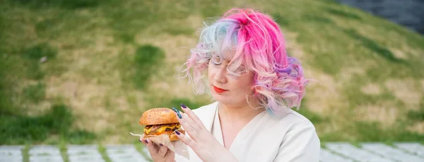 Caucasian woman with curly colored hair eating burger. Bad eating habits and love of fast food.