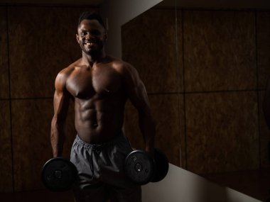 Kas yığını koyu tenli adam dambıllarla egzersiz yapıyor.