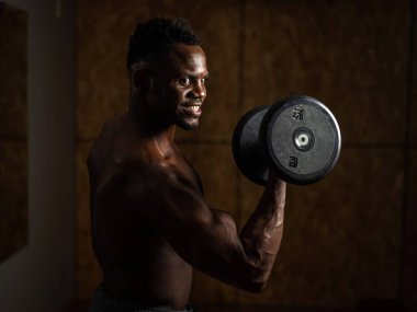 Çekici Afrikalı Amerikalı adam gülümsüyor ve halterlerle egzersiz yapıyor.