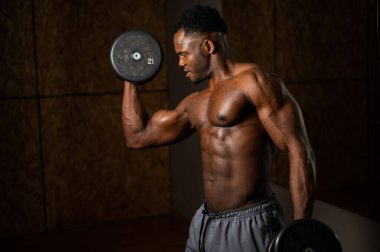 Çekici Afrikalı Amerikalı adam gülümsüyor ve halterlerle egzersiz yapıyor.
