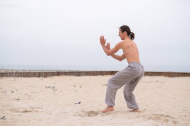 Kafkasyalı, uzun saçlı, dışarıda qigong antrenmanı yapan bir adam.