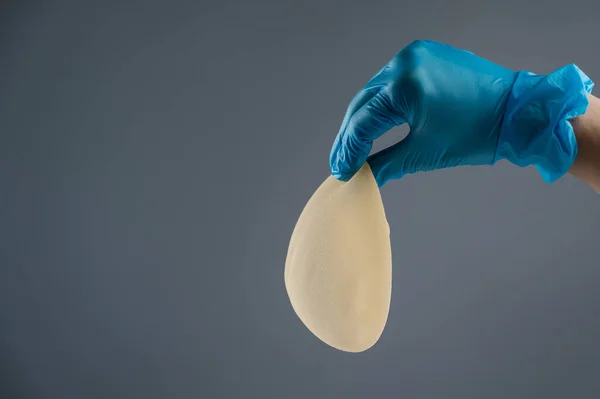 Kvinnlig Hand Handskar Håller Tårdropp Formade Bröst Implantat Grå Bakgrund — Stockfoto