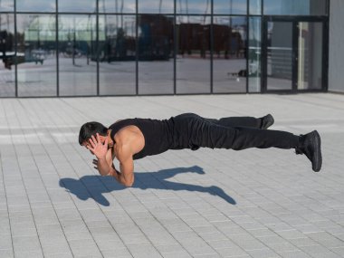 Siyah spor kıyafetli bir adam dışarıda şınav çekerken zıplıyor.