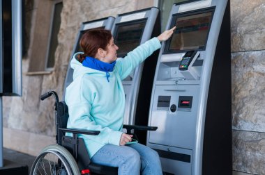 Tekerlekli sandalyedeki beyaz kadın self-servis kasasından tren bileti alıyor.