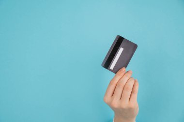 Bir kadının eli kağıtta bir delikten dışarı sarkan mavi arka planda bir kredi kartı tutar.