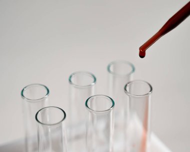 Laboratuvar asistanının beyaz arka plandaki bir test tüpüne kan damlatırken yakın plan fotoğrafı.