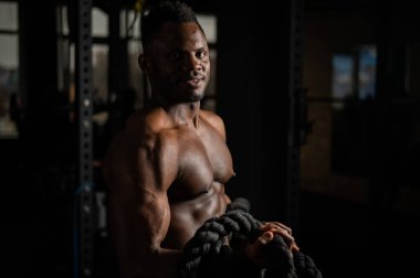 Kaslı Afrikalı Amerikalı adam spor salonunda iple poz veriyor.