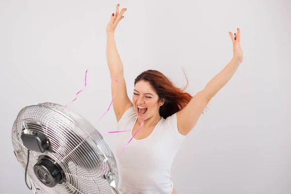 Joyful caucasian woman enjoying the wind blowing from an electric fan on a white background