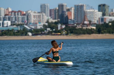 Beyaz bir kadın şehirdeki nehirde SUP sörfüne biniyor. Yaz sporu