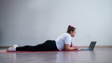 Genç Artı Boyutlu Kadın İnternet 'te esniyor. Esnek kız yoga yapıyor ve internetten dizüstü bilgisayarda ders izliyor..