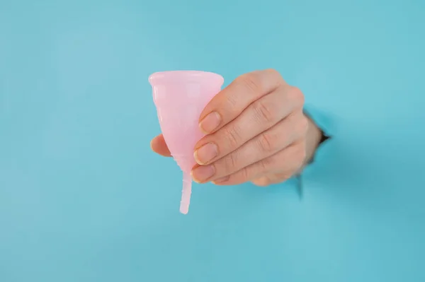 Egy Kék Hátterű Lyukból Kilógó Női Kéz Rózsaszín Menstruációs Poharat — Stock Fotó