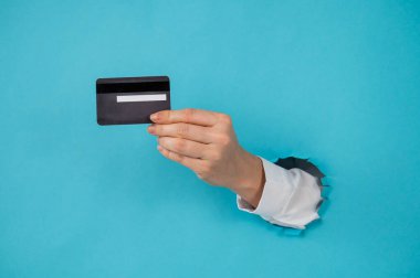 Bir kadının eli kağıtta bir delikten dışarı sarkan mavi arka planda bir kredi kartı tutar.