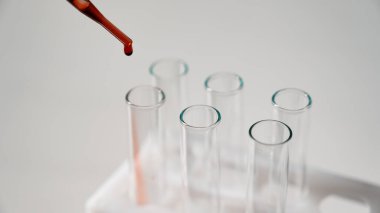 Laboratuvar asistanının beyaz arka plandaki bir test tüpüne kan damlatırken yakın plan fotoğrafı.
