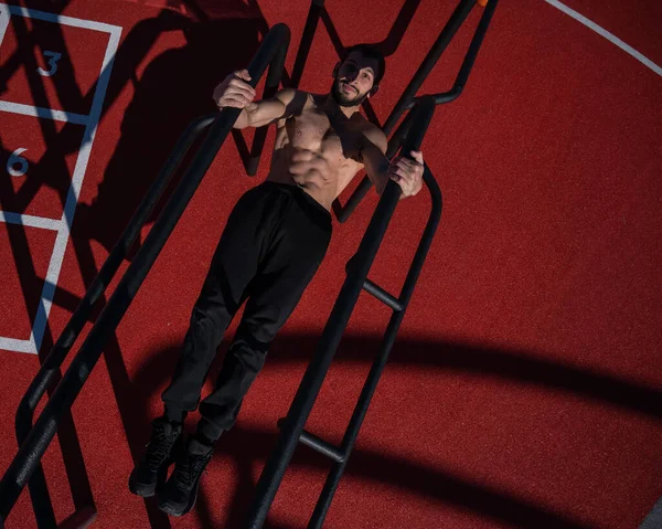 Shirtless man doing balance on uneven bars outdoors. View from above