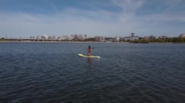 Beyaz bir kadın şehirdeki nehirde SUP sörfüne biniyor. Yaz sporu