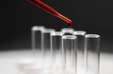 Laboratuvar asistanının, pipetten kan damlatarak test tüpüne kan damlattığı yakın plan.