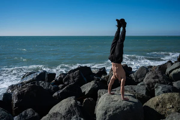 Tişörtsüz Bir Adam Deniz Kenarındaki Kayalarda Amuda Kalkıyor — Stok fotoğraf