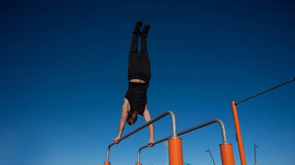 Shirtless man doing handstand on parallel bars at sports ground