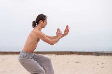 Kafkasyalı, uzun saçlı, dışarıda qigong antrenmanı yapan bir adam.