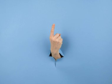 Bir kadının eli mavi arka planda bir delikten dışarı sarkan işaret parmağını gösterir.