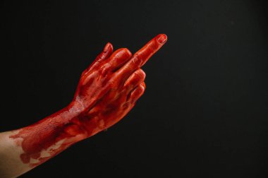 Kana bulanmış kadın eli siyah bir arka planda orta parmağı gösteriyor.