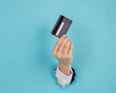 Bir kadının eli kağıtta bir delikten dışarı sarkan mavi arka planda bir kredi kartı tutar.