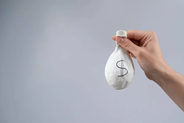 A woman is holding a deflated balloon with a dollar sign. The concept of an inflated currency value