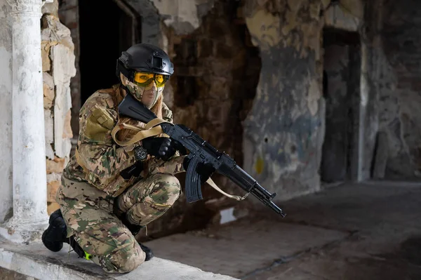 Portrait of a woman in a helmet and goggles with a machine gun in her hands. A female soldier in a camouflage uniform holds a weapon