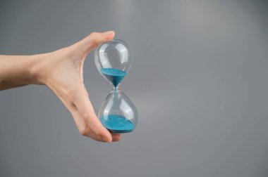 Gri arka planda kum saati tutan bir kadın. Yakın plan. Boşluğu kopyala